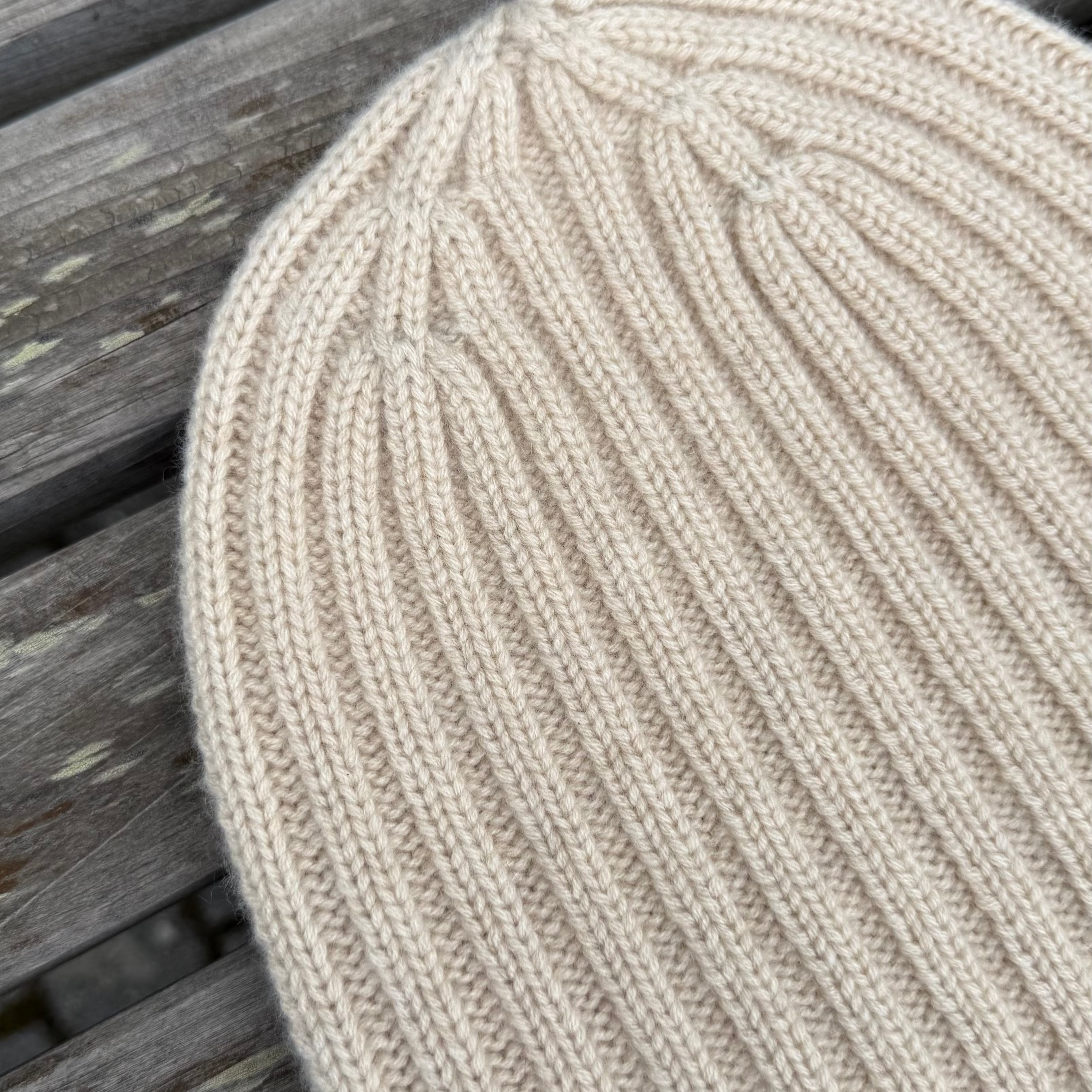 Close-up of an undyed knitted beanie on a wooden surface