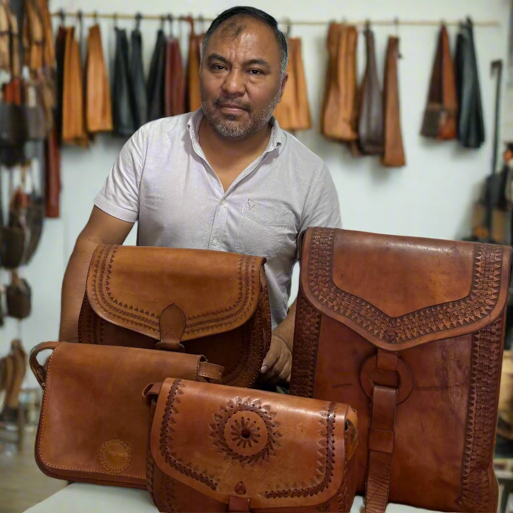 A man is standing at his workstation and presenting his handmade leather handbags with various leather materials in the background.