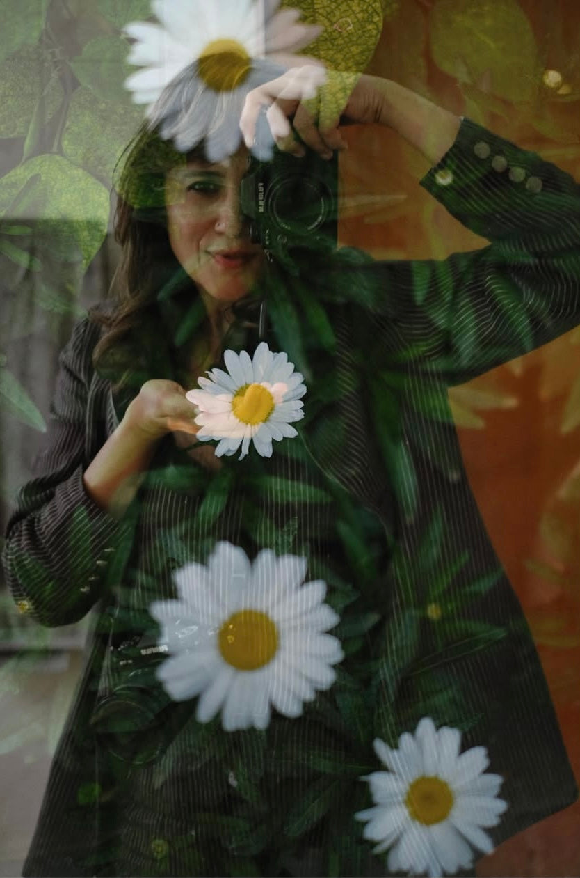 A woman is taking a self-portrait in an artistic way with white daisy flowers in the foreground.