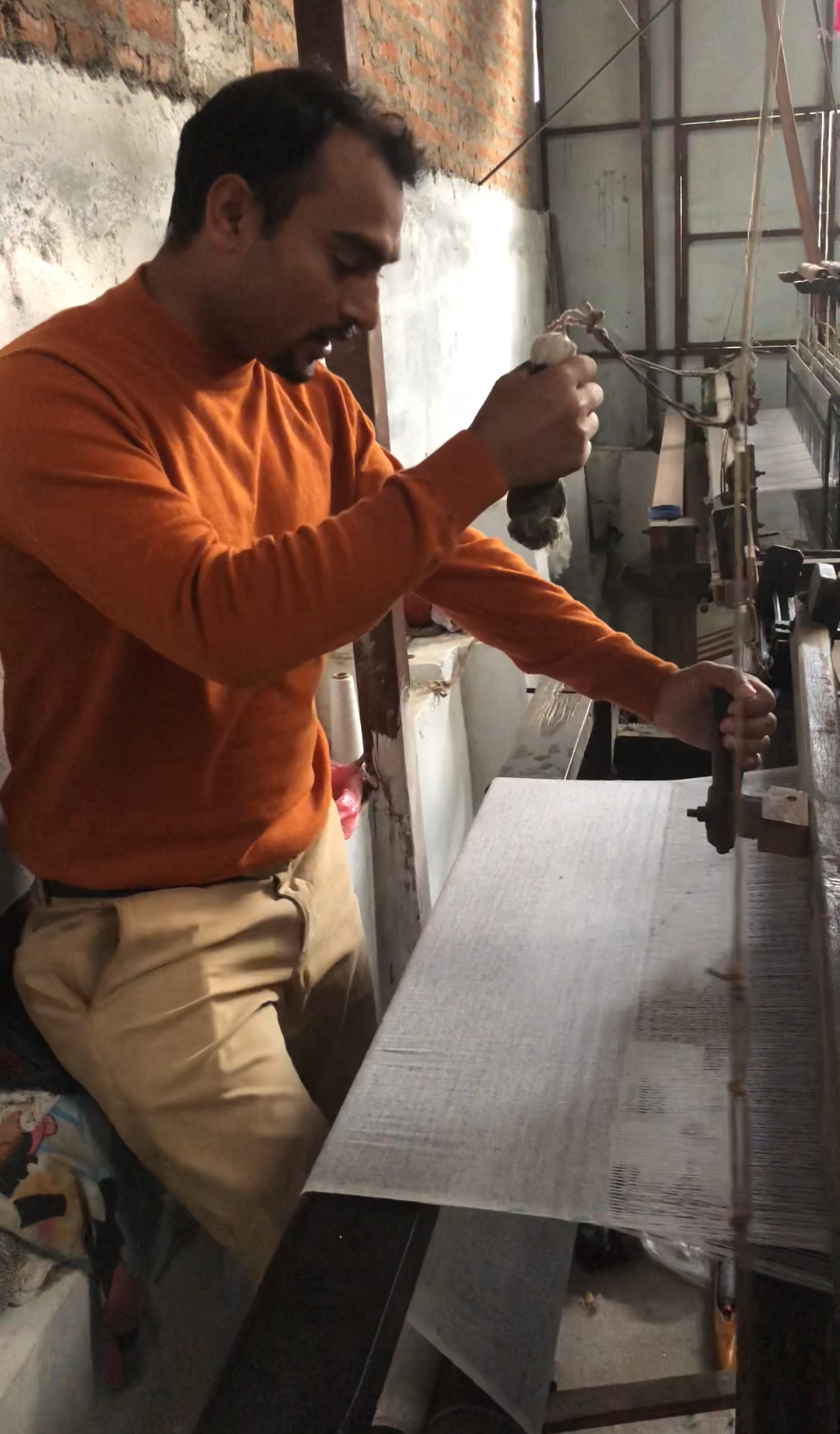 Man in an orange sweater using a hand loom in a workshop.