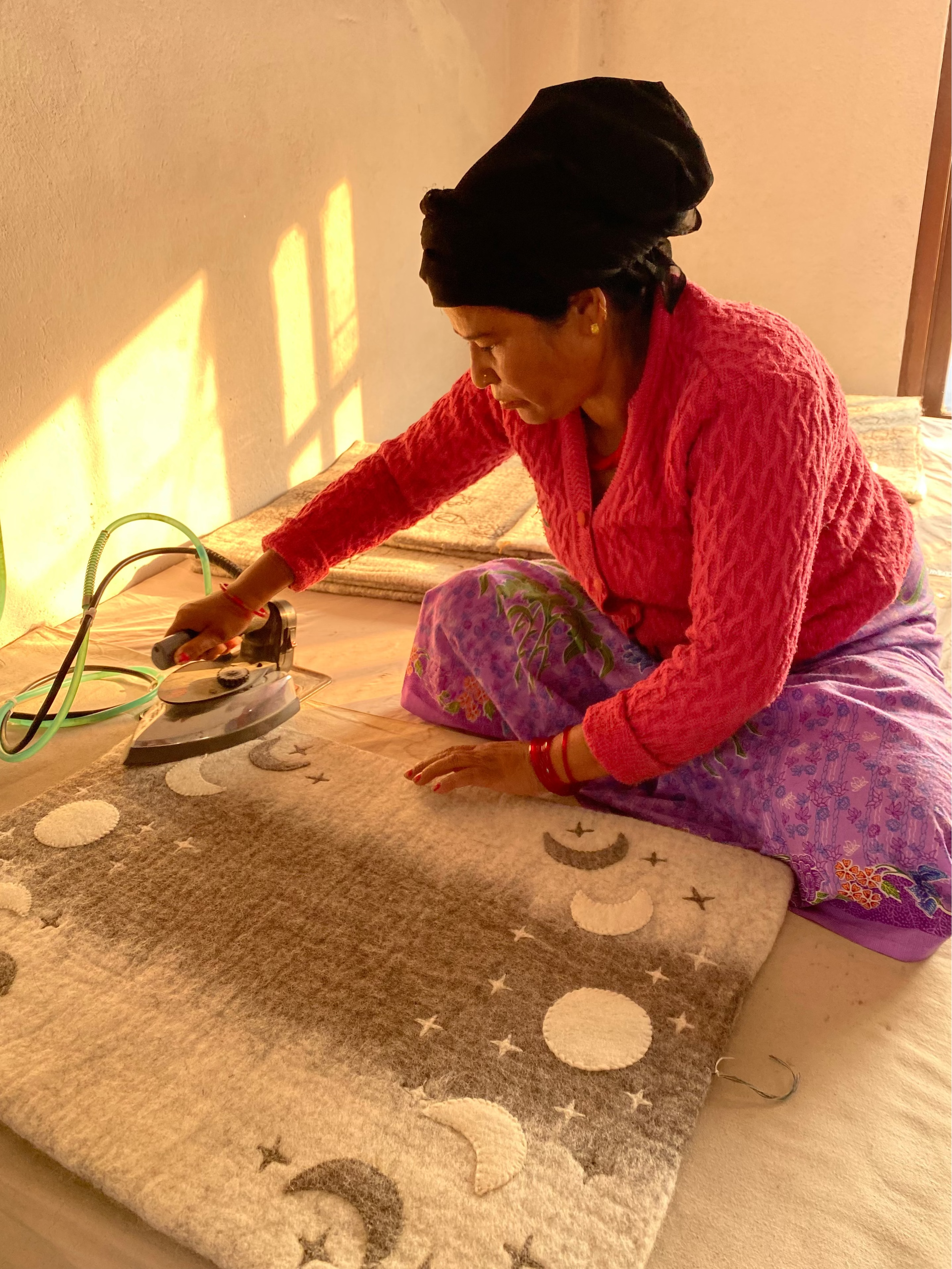 Woman ironing a wool mat with star and moon patterns on a platform.