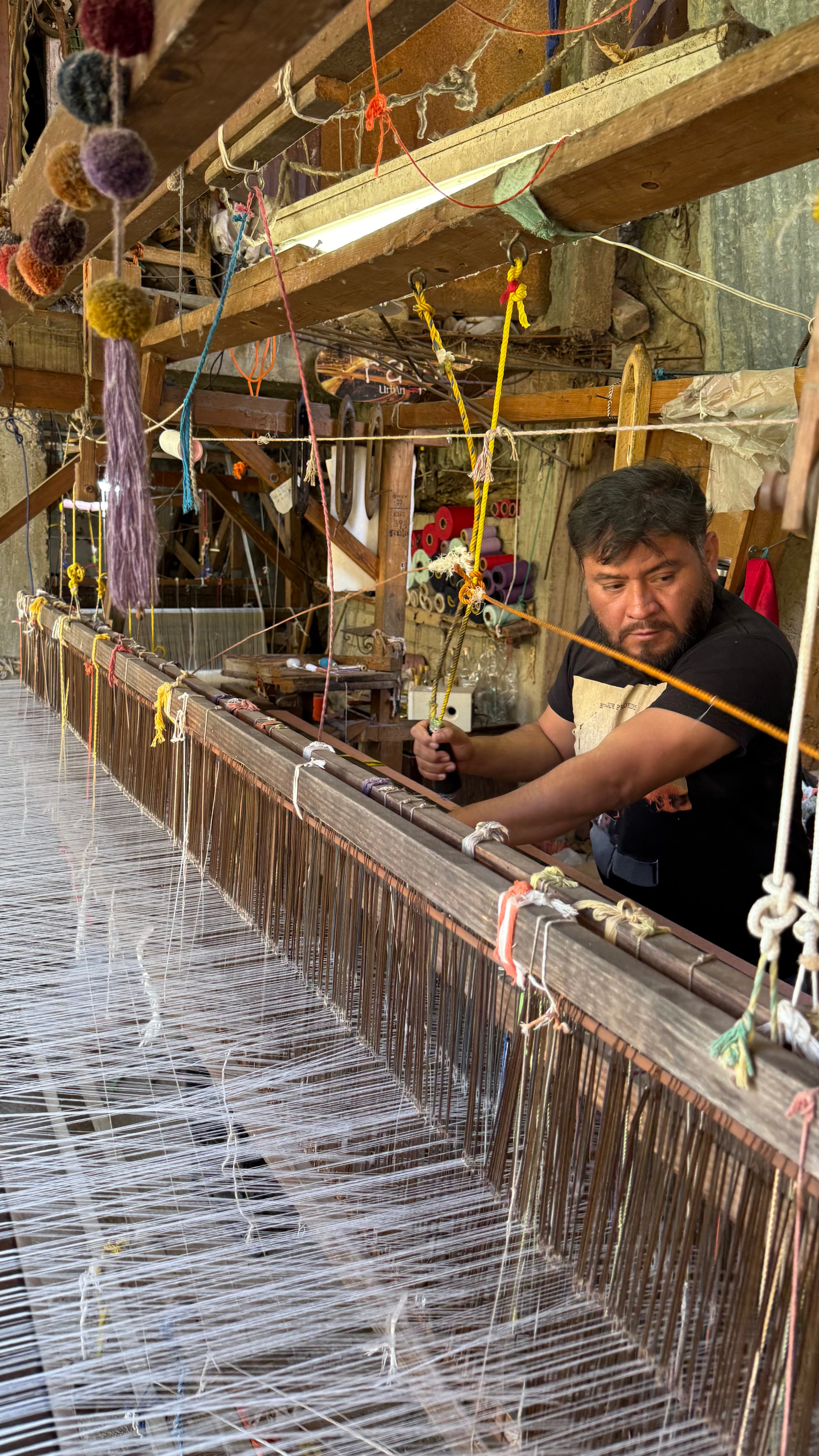 Man working with a large wooden loom in a workshop.
