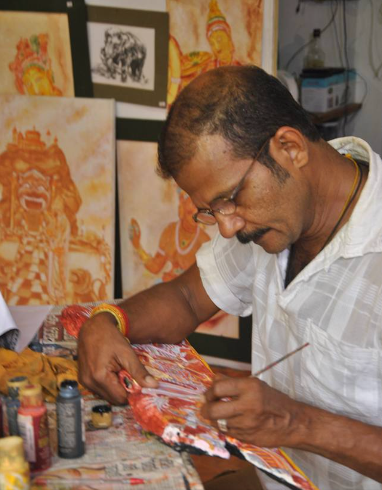 Man painting with various materials and artworks in the background.